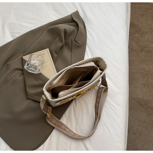 Detail of white tote bag interior compartments and floral woven strap on white bedding