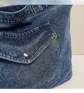 Detail of dark blue denim tote bag showing twill texture and pocket with silver metal button