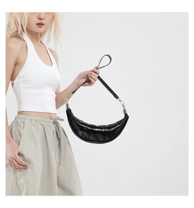 Detail view of black glossy crescent bag featuring golden hardware on a shoulder strap