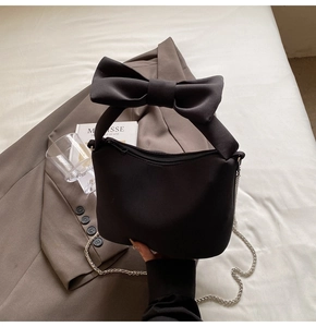 Detail view of the oversized black bow handle and metal chain on this crossbody handbag