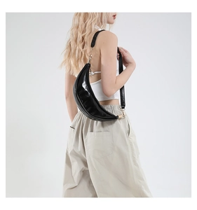 Close-up of black glossy patent leather crescent bag worn as a stylish shoulder bag