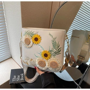 Detail view of sunflower embroidery and woven shoulder strap on beige crossbody bag