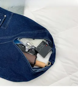 Detail view of deep blue denim hobo bag capacity showing sunglasses, perfume and umbrella