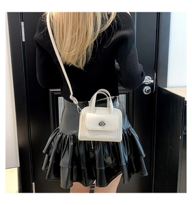 Detail of a creamy white handbag with silver twist lock and adjustable crossbody strap