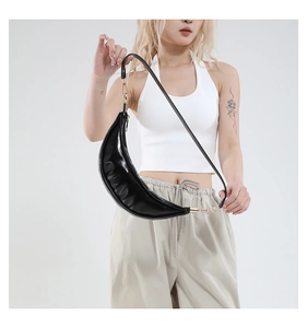 Detailed view of high-gloss black crescent bag featuring golden hardware and zippers