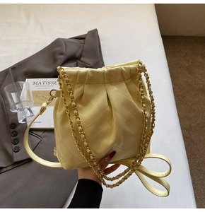Detailed close-up of quilted beige bucket bag with gold chain strap and leather handle