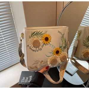 Close-up of white crossbody bag featuring embroidered sunflowers and woven strap