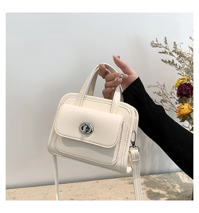 Close-up of minimalist cream white briefcase bag with silver twist lock and fine stitching