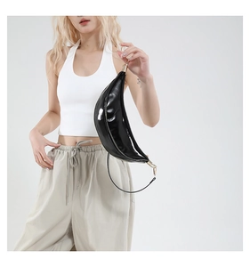 Detail shot of a glossy black patent leather crescent bag on model with gold zipper