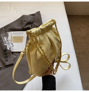 Detail of light yellow quilted shoulder bag featuring gold chain and leather bow decoration