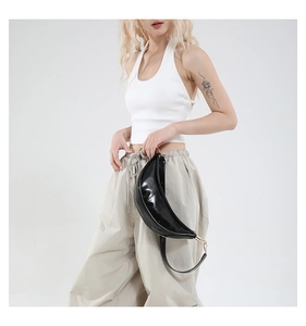 Detail of a black glossy crescent-shaped crossbody bag with a wide adjustable strap