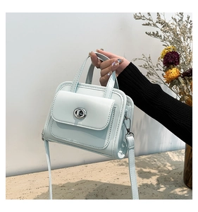 Macro detail of a light blue glossy leather handbag with a silver twist-lock fastener