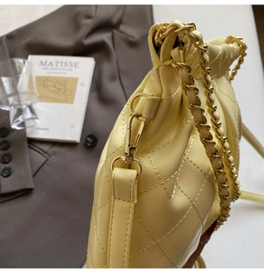 Detail of cream quilted leather handbag with gold chain strap on a grey suit background