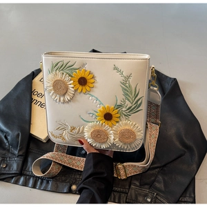 Detail of white PU leather crossbody bag featuring floral embroidery and ethnic woven strap