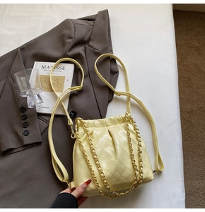 Detail of light yellow quilted bucket bag featuring a gold chain and drawstring closure
