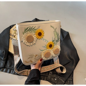 Close-up of floral embroidery on a white crossbody bag with woven shoulder strap