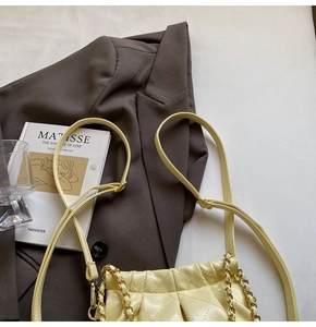 Close-up of light yellow quilted chain bag with ruching detail on brown blazer