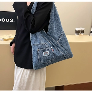 Detail view of washed blue denim tote bag with side pocket and woven rainbow patch logo