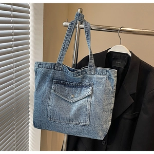 Detail of blue denim tote bag featuring a metal button flap pocket and sturdy handles