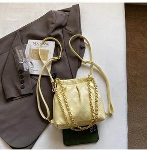 Detail view of yellow quilted bucket bag with golden chain and drawstring closure