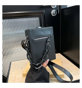 Detail of black lizard-embossed box bag with decorative chain and industrial style