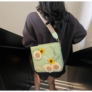 Detail of floral embroidery and woven strap on green crossbody bag worn by model