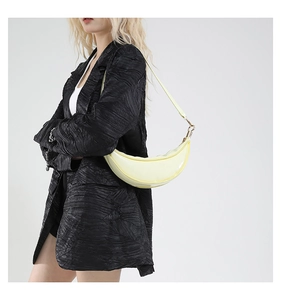Close-up of a pale yellow crescent dumpling bag worn by a model in a minimalist setting