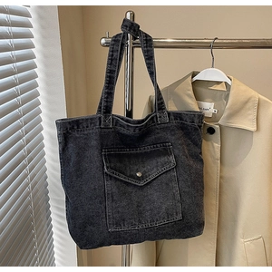 Macro detail of vintage black denim tote bag featuring a large front flap pocket