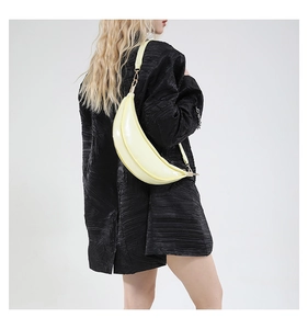 Pale yellow crescent bag in glossy patent leather shown on a model's shoulder