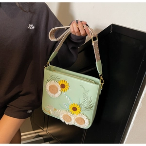 Detailed embroidery of sunflower and daisy on a green crossbody bag with woven strap