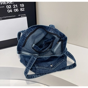 Detail view of denim tote bag showing interior zipper pocket and outer flap pocket
