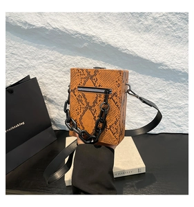 Detailed view of orange-brown python pattern handbag with chunky black plastic chain and strap