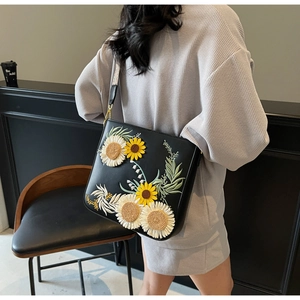 Detail view of sunflower embroidery on a black leather crossbody bag with golden buckle