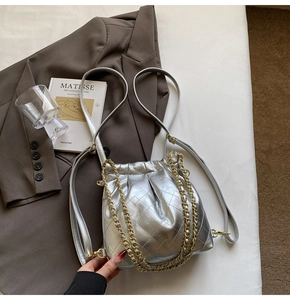 Detail of silver metallic quilted drawstring bucket bag with gold chain and brown blazer