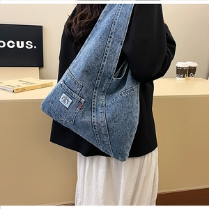 Detail of blue washed denim tote bag showing functional side pocket and retro woven label