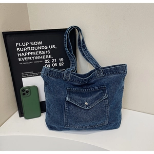 Detail of dark blue denim tote bag featuring a front flap pocket with a metal snap button