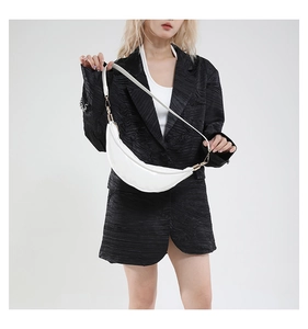 Detail of white half-moon leather crossbody bag with gold hardware on a black suit jacket