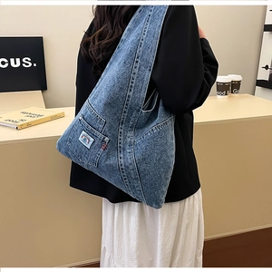 Detail view of the washed blue denim shoulder bag featuring a side pocket and woven tag