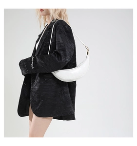 Detail of white crescent shoulder bag on model showing sleek leather and gold hardware