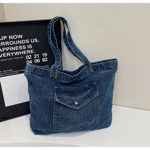 Detailed close-up of dark blue denim tote bag texture and front pocket with silver button