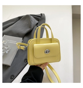 Macro shot of yellow leather crossbody bag featuring a silver twist lock and smooth handle