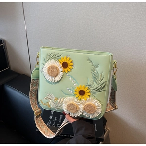 Detail of sunflower embroidery on a light green leather crossbody bag with woven strap