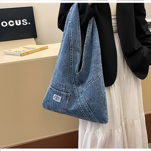 Detail view of washed denim tote bag showing triangular shape and colorful logo patch