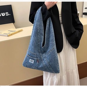 Detail of blue denim tote bag featuring a front pocket with rainbow logo and asymmetrical design