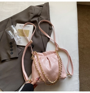 Detail of light pink quilted bucket bag with golden chain strap on a white background