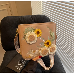 Detail showing high-quality sunflower embroidery and woven strap on beige shoulder bag
