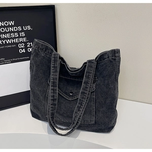 Detail of vintage washed black denim tote bag with white stitching and front metal buckle pocket