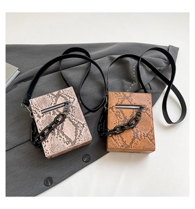 Detail of snake skin texture crossbody bags with decorative chains on grey fabric