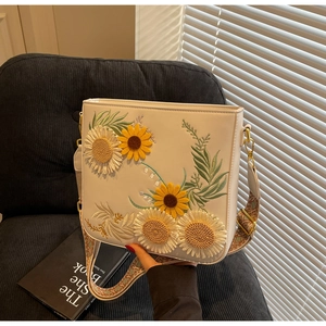 Detail of sunflower embroidery and bohemian strap on an off-white crossbody bag