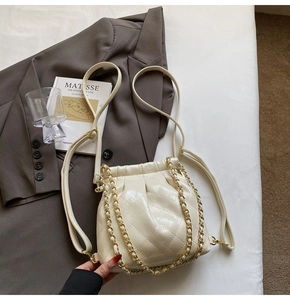 Detailed view of quilted beige bucket bag with chain strap on minimalist background